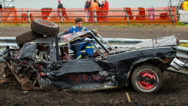 A man exits a destroyed derby car.