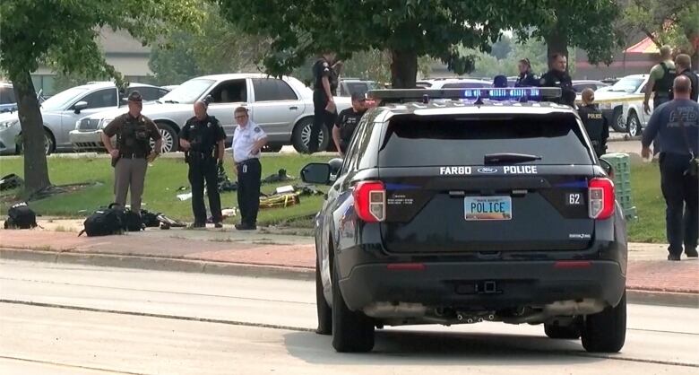 A police vehicle is parked in the street while police officers stand around in the background.