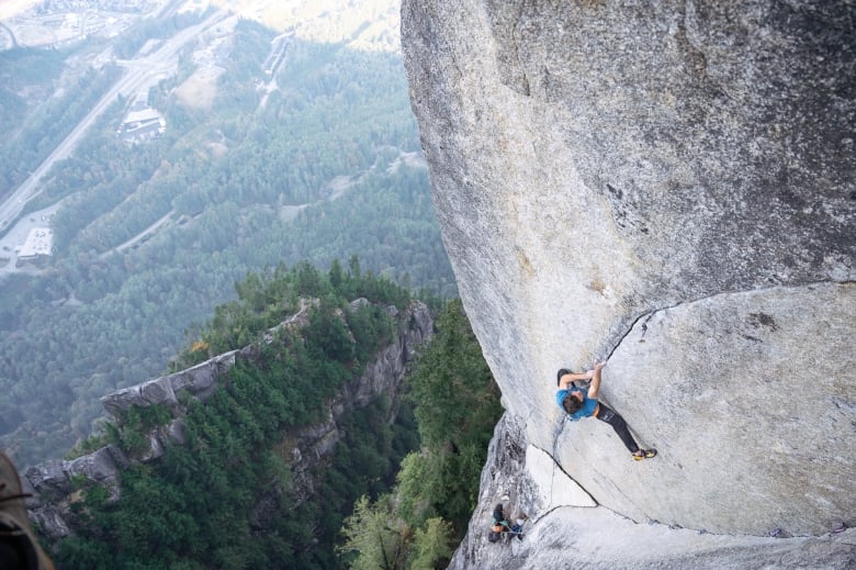 A man climbs up a small crack on a sheer rockface.