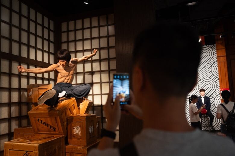 A man takes a picture of a wax figure in a fighting pose at a museum.