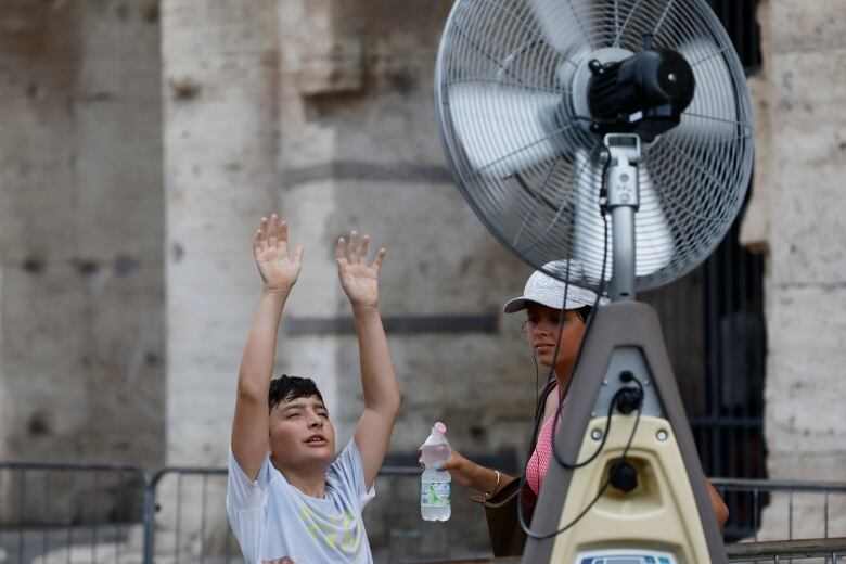 A boy cools off, in front of a large fan, near the ancient Colosseum, in Rome, Italy.