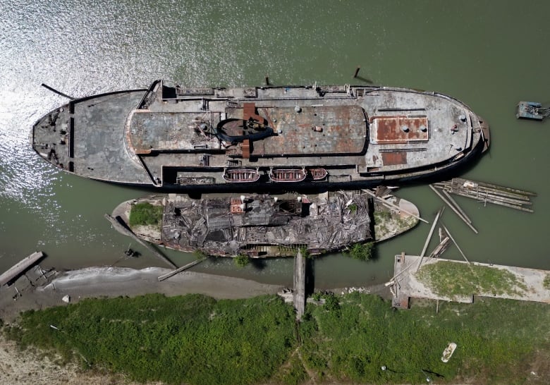 Two abandoned, dilapidated boats moored on a river in an aerial shot taken directly above.