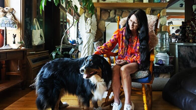 A woman sits in a rocking chair petting a dog.