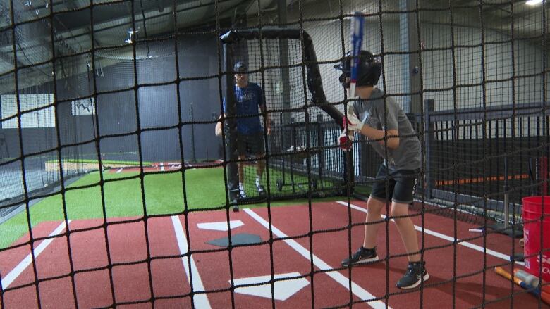 A boy standing in a batters box holding a baseball bat. A pitcher is in the background. 