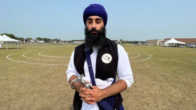 A man wearing a turban stands in a field holding a sword.