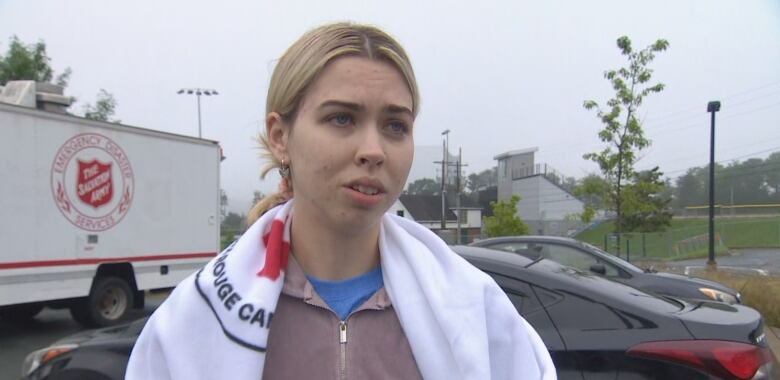 A woman stands outside wearing a blanket from the Canadian Red Cross over her clothes.