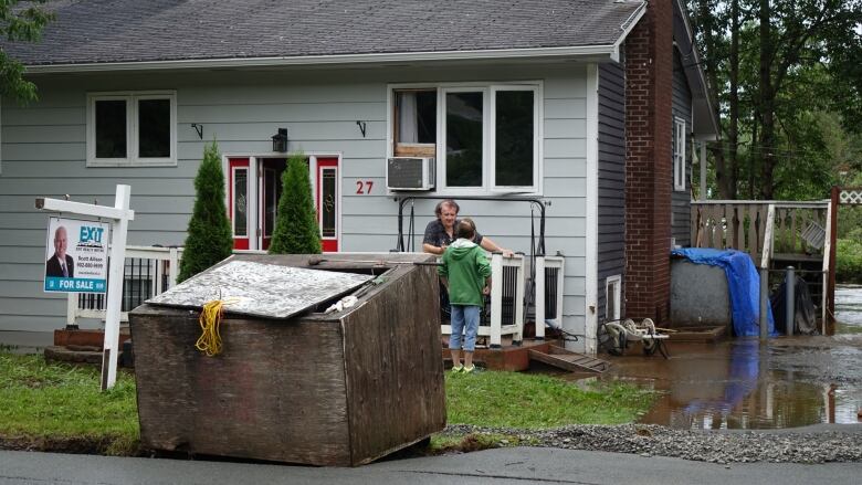 A man stands outside his home talking to another person. Water is visible around part of the foundation of the home