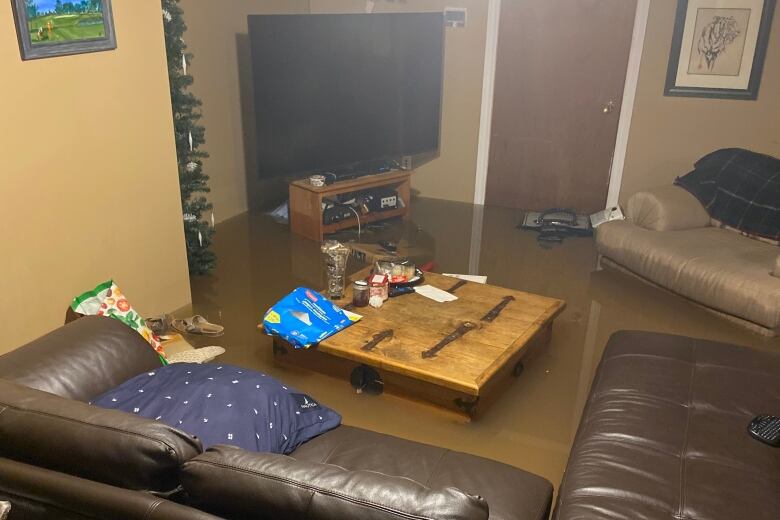 Water surrounds a table, TV stand and couch in a flooded basement.