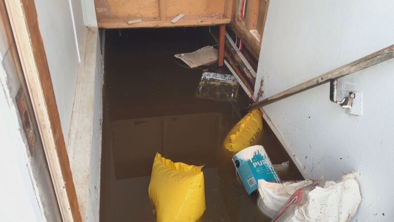 looking down a set of flooded stairs. A paint can and a few bags float in the dark brown water.