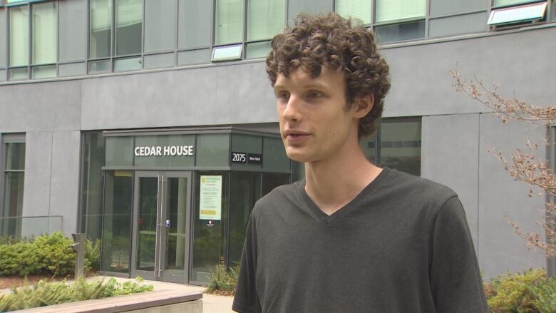 A young man stands in front of a student residence building. 