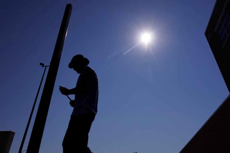 A man, photographed from below, is silhouetted by the glaring sun.