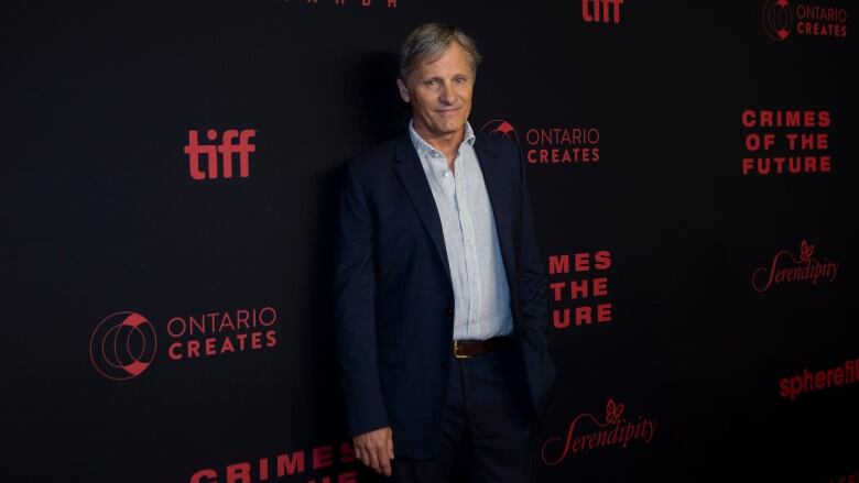 A man wearing a navy blue jacket and light blue dress shirt poses at an event.