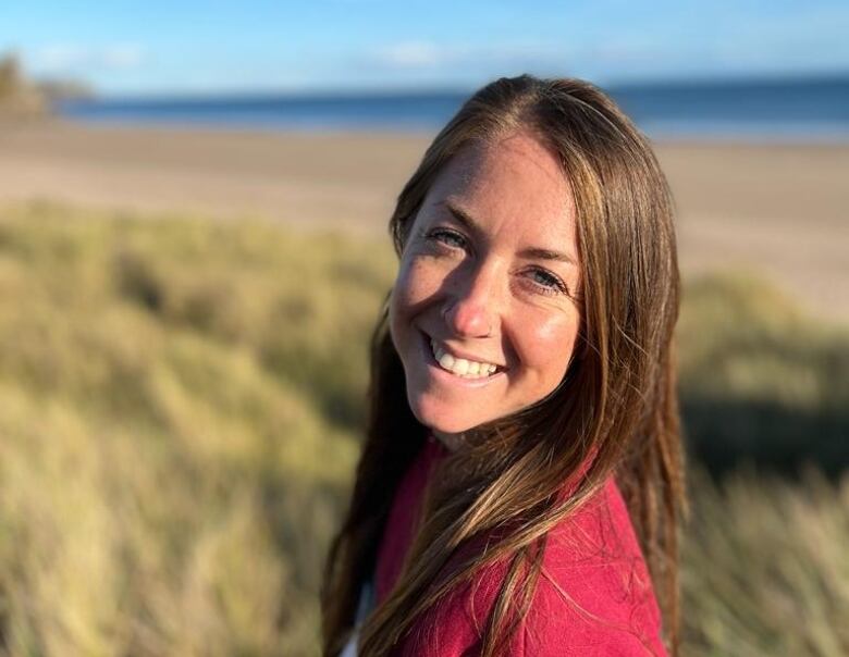 A woman with long hair stands on the beach and smiles.