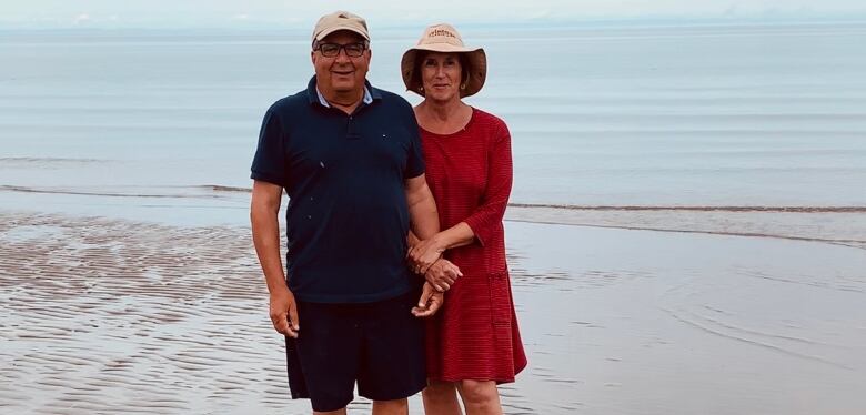 A man and woman with their arms entwined at the water's edge on a beach.