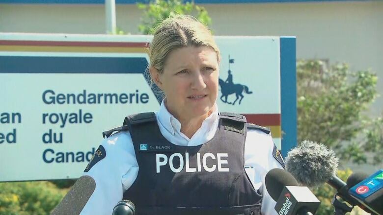 A woman wearing a police vest stands in front of an RCMP sign.