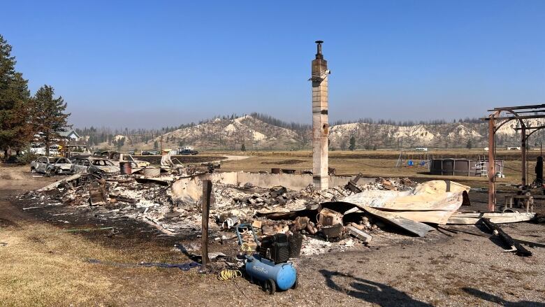 A chimney stands above the charred remains of a house. Dusty dry hills can be seen in the background.