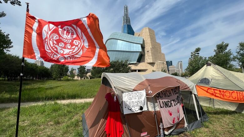 A tent with a red dress hanging from it sits in a field next to another tent.