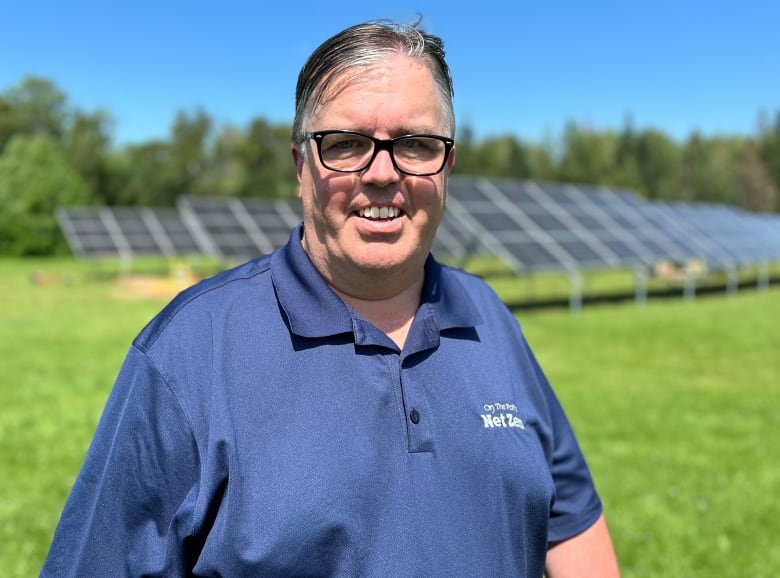 Steven Myers outside in summer in front of a field of solar panels.