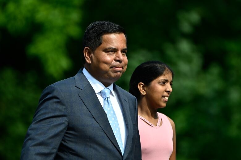 A politician and his daughter walking with trees in the background.