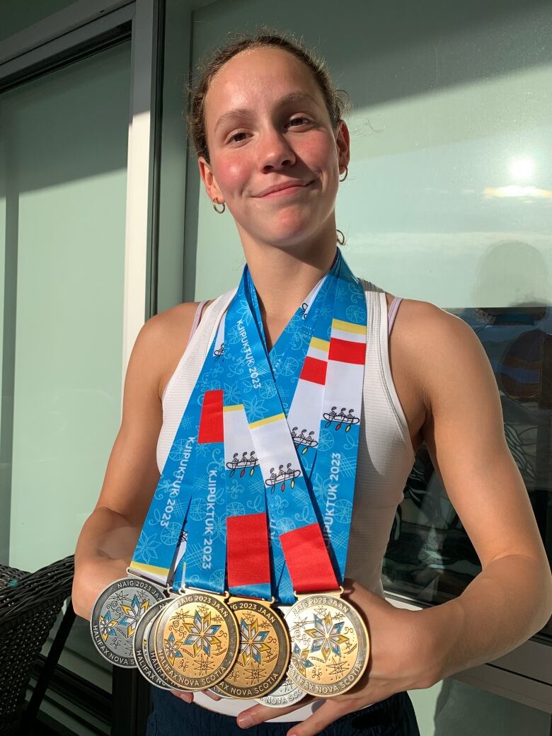 A young woman smiles while wearing multiple medals around her neck.