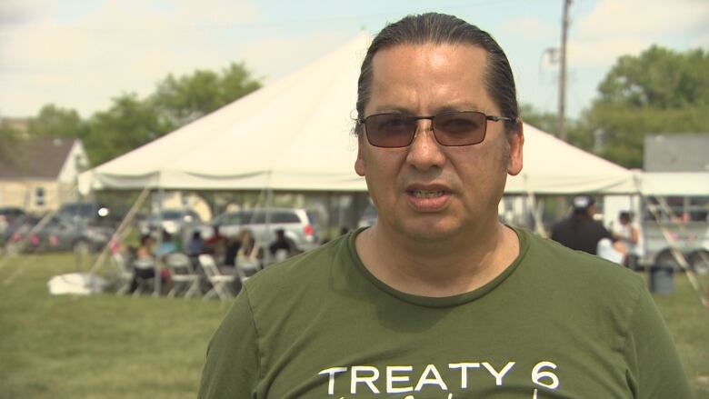 A man wearing sunglasses and a Treaty 6 T-shirt with his hair pulled back faces the camera.