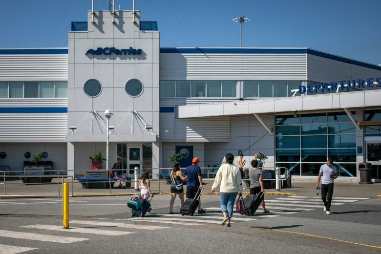 People are pictured wheeling suitcases on their way to a B.C. Ferries terminal.