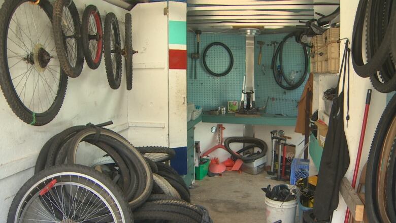 Bike wheels hang on the walls inside a cargo trailer, with other repair supplies contained in buckets on the floor.