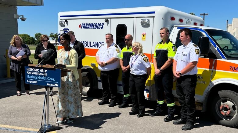 A woman speaks from a podium while surrounded by healthcare workers. 