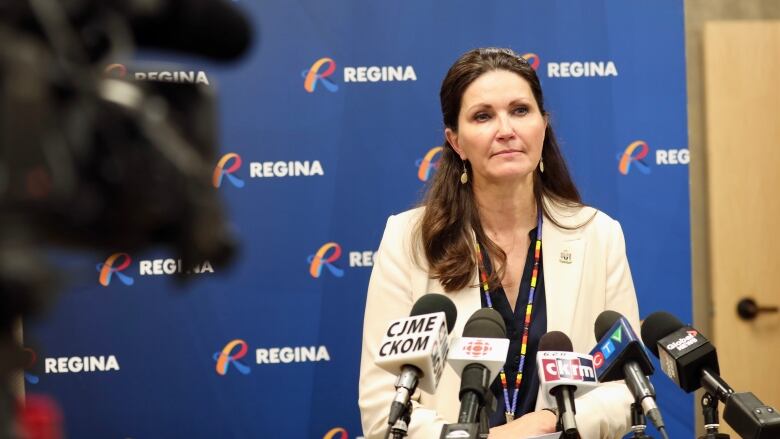 A woman stands at a podium with many microphones in front of her.