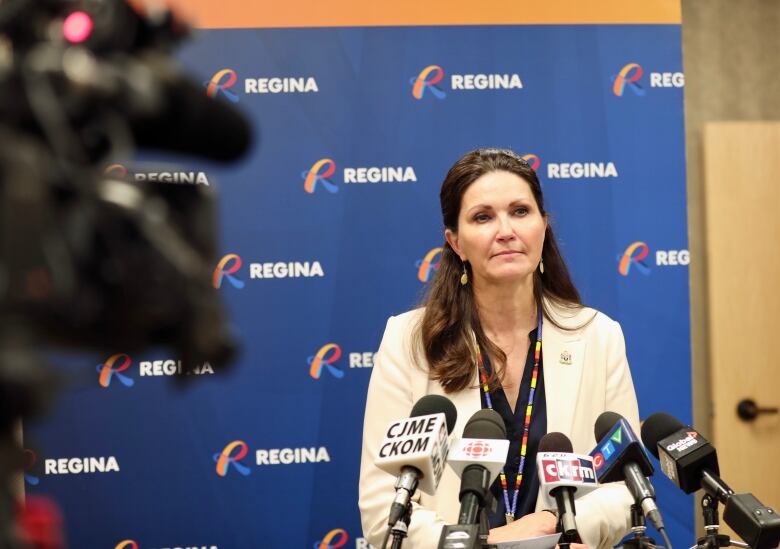 A woman stands at a podium with many microphones in front of her.