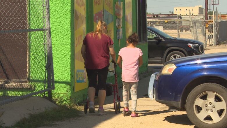 Woman with a walker, left, and a young girl in a pink shirt, right, walk together toward a convenience store, with their backs to the camera.