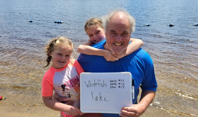 David kneals at the water's edge holding a white board that reads 