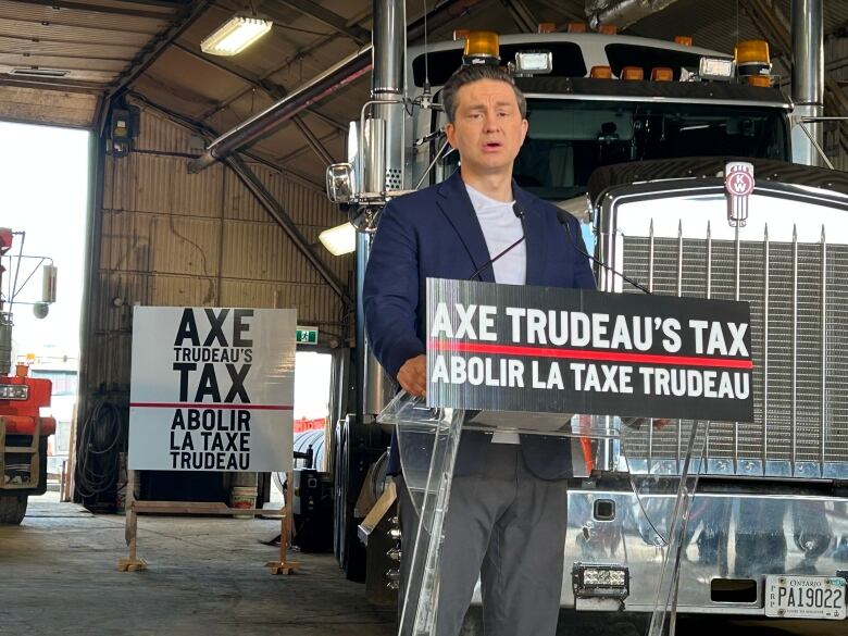 A man speaking on a podium in front of a big truck.