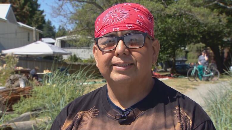 A man wearing glasses and a red bandana stands near an archaeological dig site