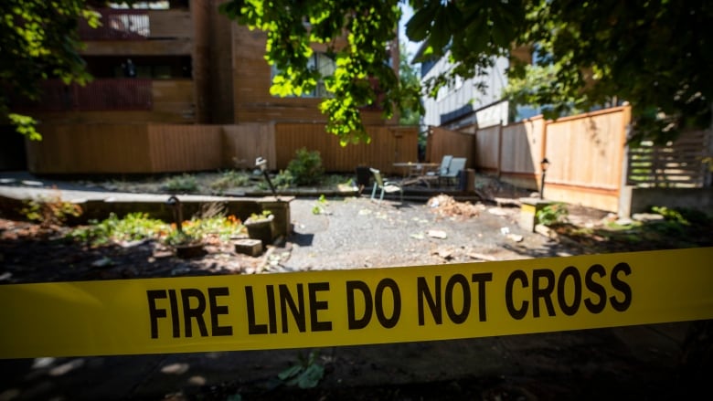 Yellow caution tape reads: Fire Line Do Not Cross. Behind it is debris scattered around an open space leading to an apartment building.