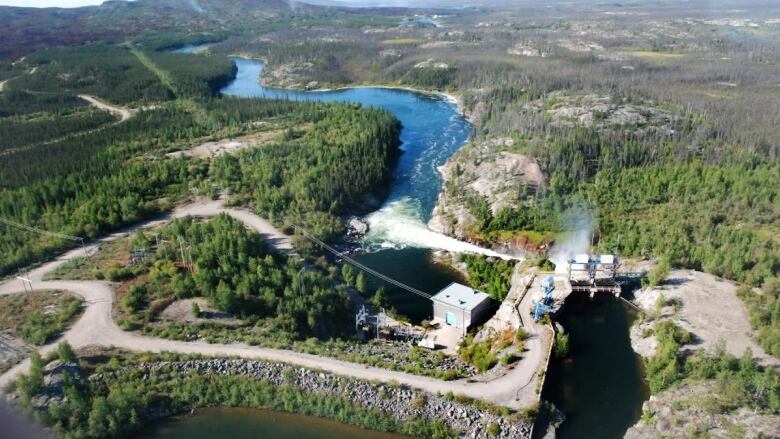 A picture of a hydro plant a zoomed out shot showing the water and greenery. 