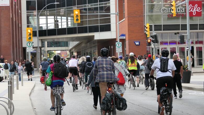 People on bikes cycle down a street lined with buildings.