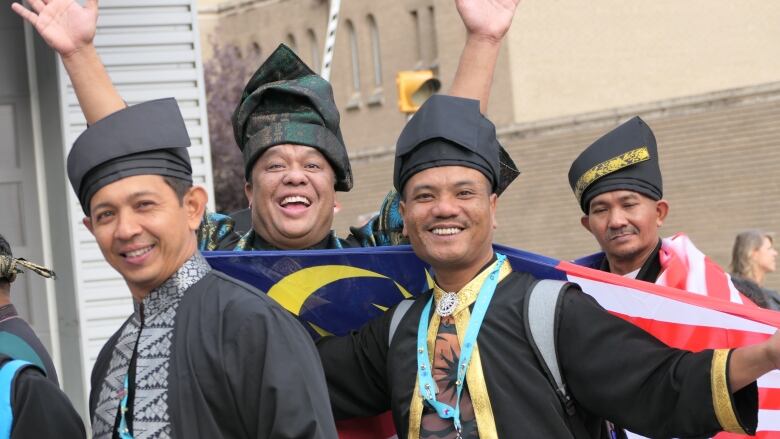 A man holds up the Malaysia flag while smiling at the camera in a crowd of people.