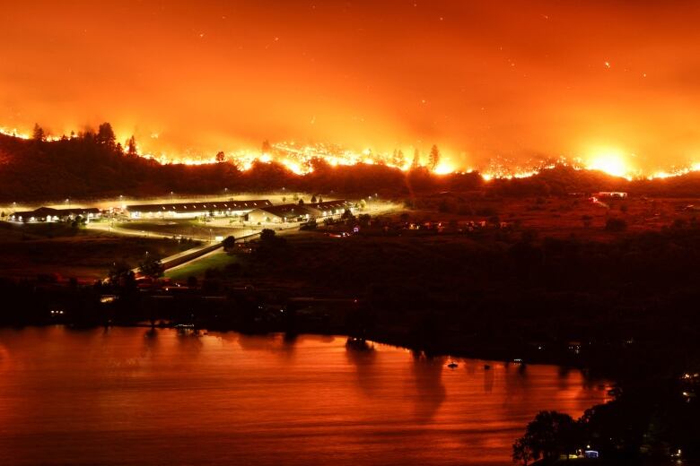 Plumes of smoke and pockets of flame dot the horizon, with orange reflections visible on water near some hills.