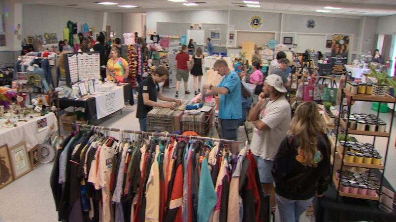 People mill about a sales floor with as number of tables, booths and racks selling clothing, toys and other items.