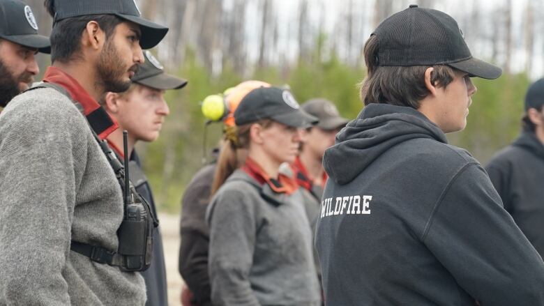 People in profile wearing hoodies and grey sweaters, some wear hard hats an protective gear.