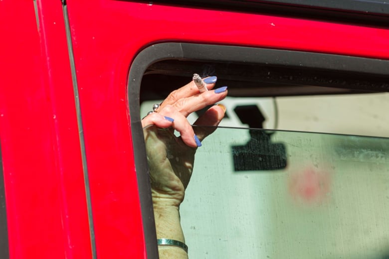 A person holds a cigarette with their finger through the crack of a car window.