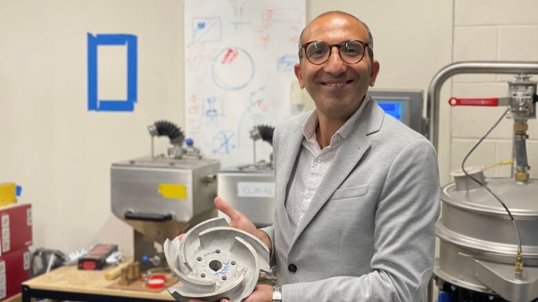 Mohsen Mohammadi pictured holding an impeller. Drawings on a whiteboard in the background