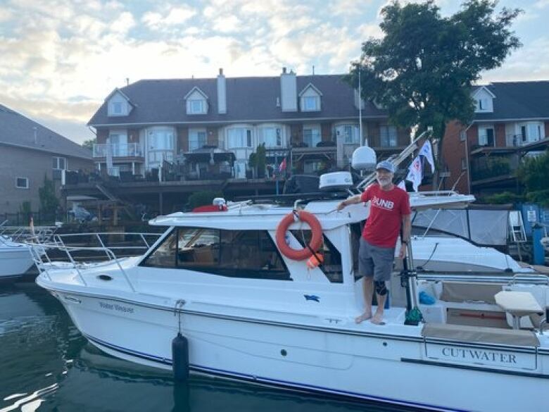 A man stands on the side of his boat and smiles at the camera as the sun goes down.