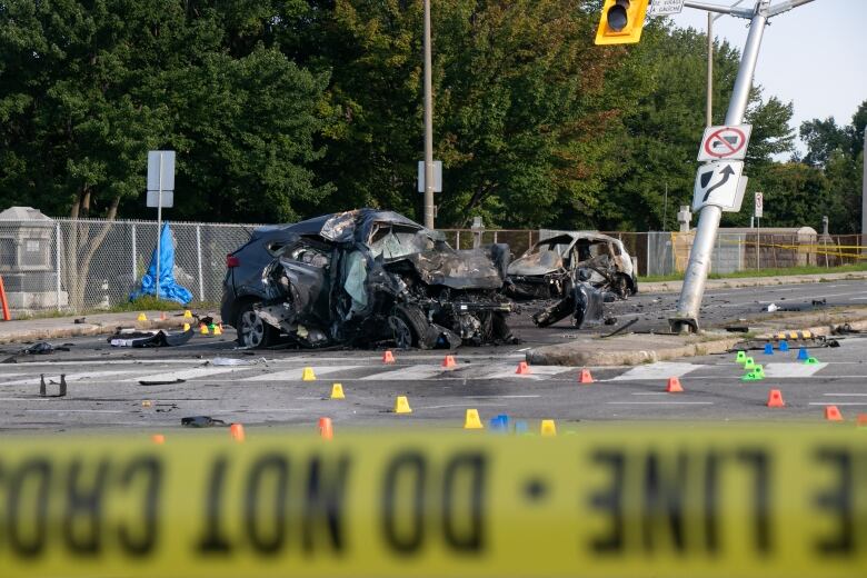 Behind a line of police tape, two cars can be seen crumpled and burned. 