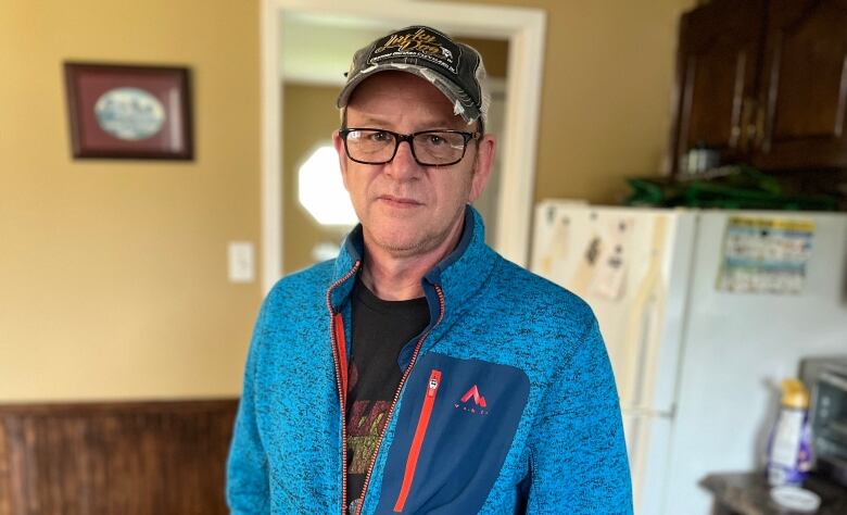 Man in blue jacket with glasses stands in kitchen