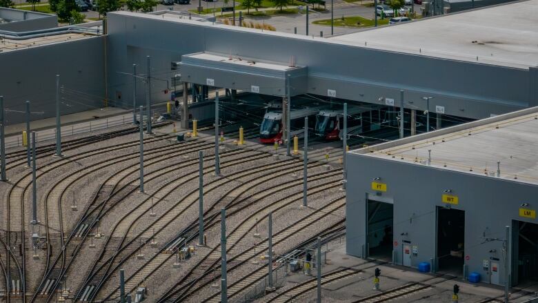 two red and white trains peek out of a large grey garage. Rail tracks lead into the garage.