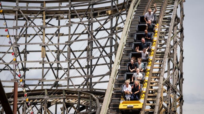 A wooden roller-coaster is pictured with people going down a drop in the yellow car. 