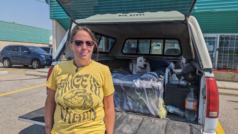 A woman standing at the back of her truck, with her dog laying on a bed inside