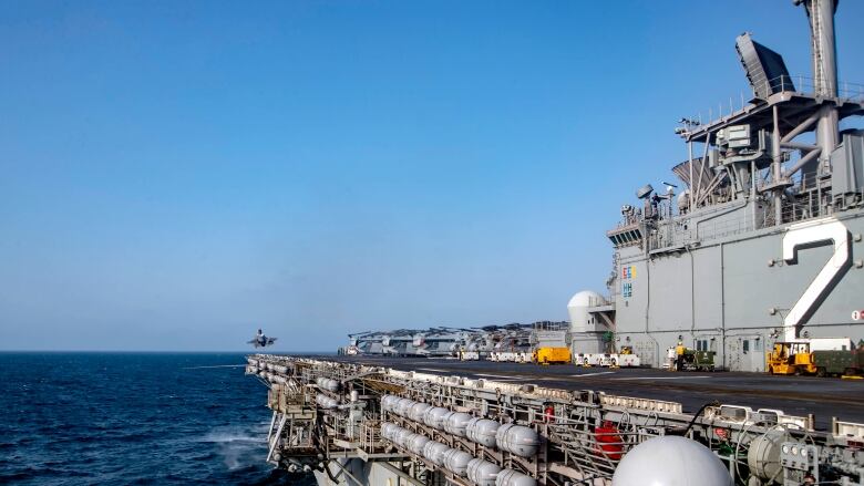 A massive warship is shown at sea, with a helicopter in the background hovering near the ship.